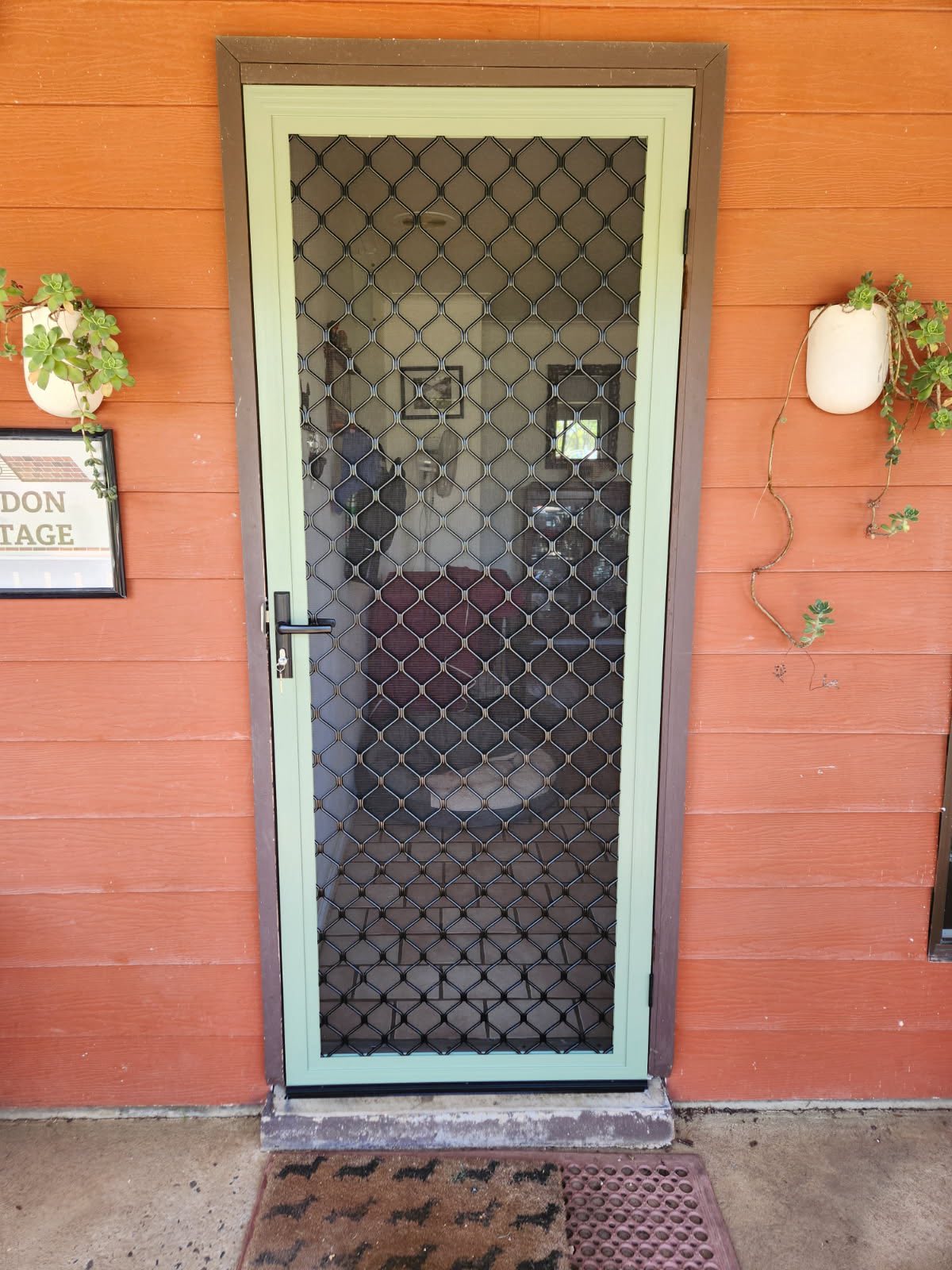 Decorative diamond grille screen door in a sage frame on an orange weatherboard cottage