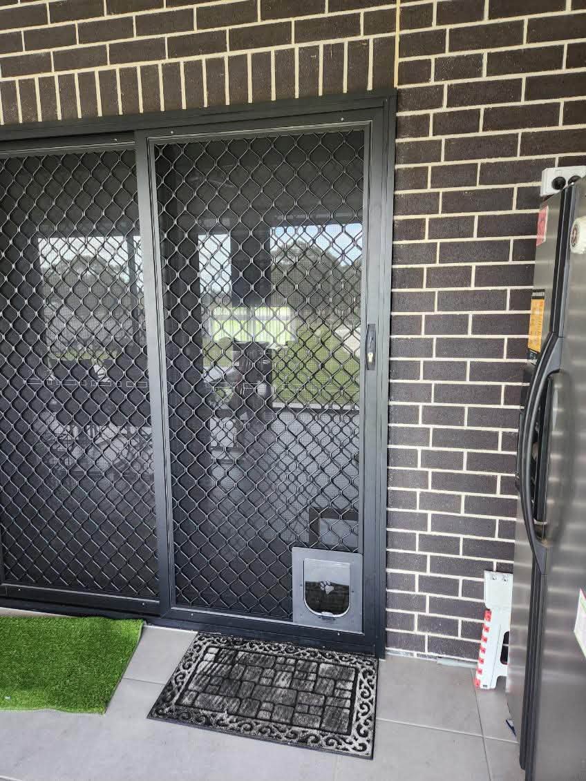 Diamond grille sliding security door with a pet door on dark brick